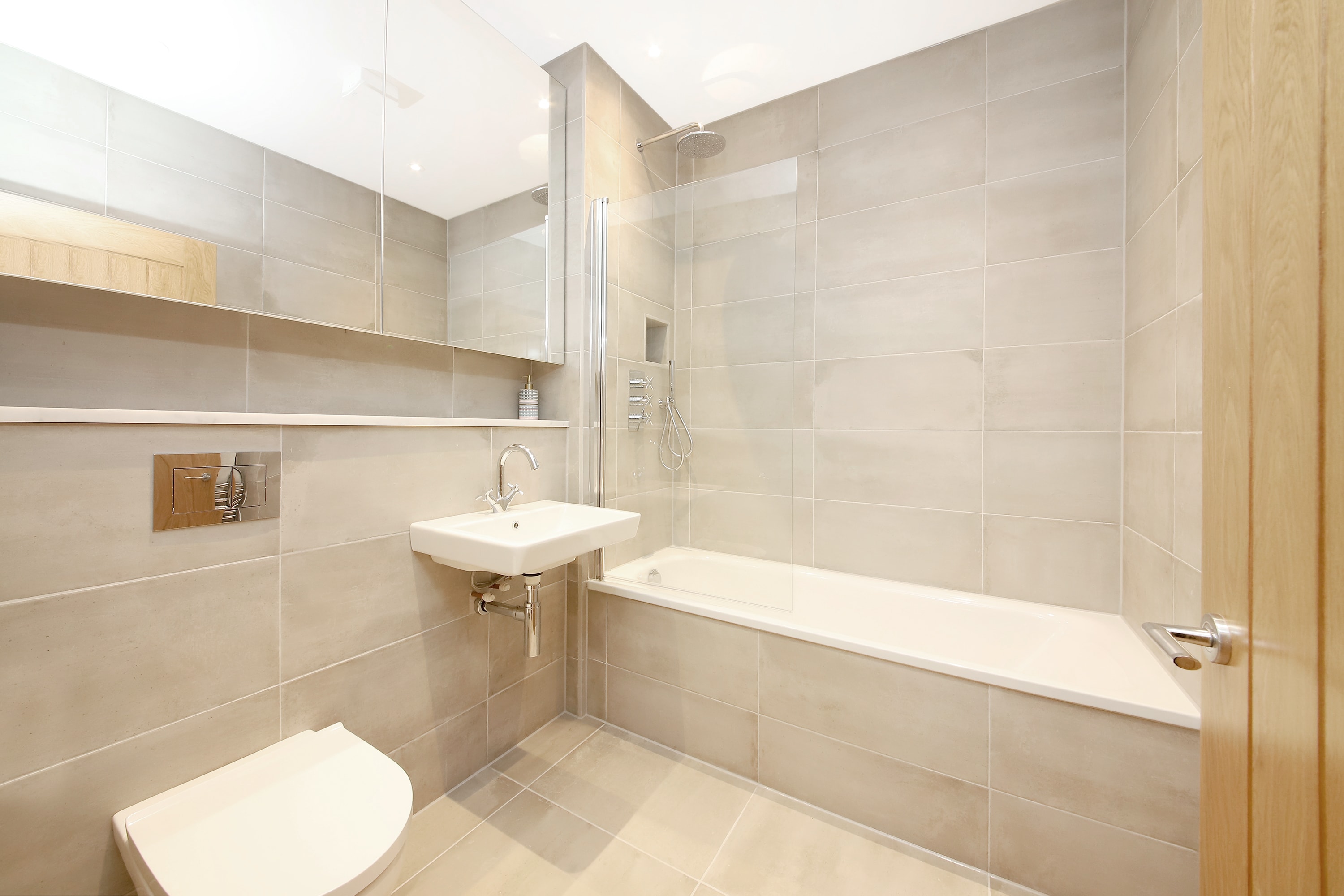 Colin Court — completed bathroom interior with full-height tiling, bath with shower, and wall-hung sanitaryware