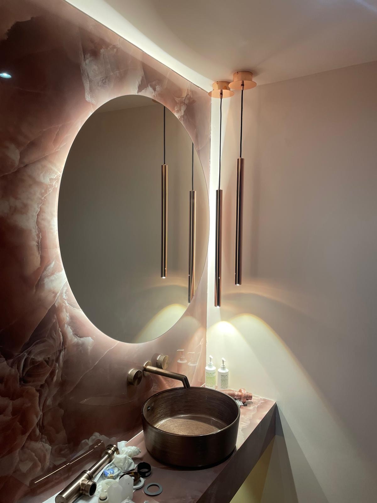 Galley Lane — luxury cloakroom with rose onyx feature wall, backlit oval mirror, copper pendant lights and black vessel sink