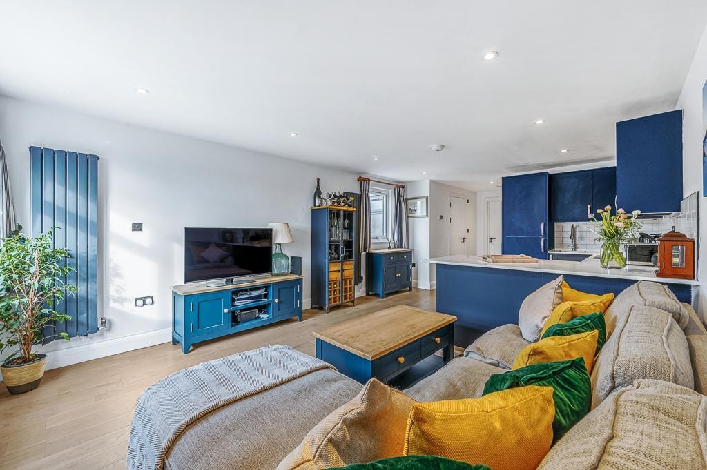 Melbourne Avenue — living room with navy radiator, TV unit and kitchen beyond, oak flooring throughout